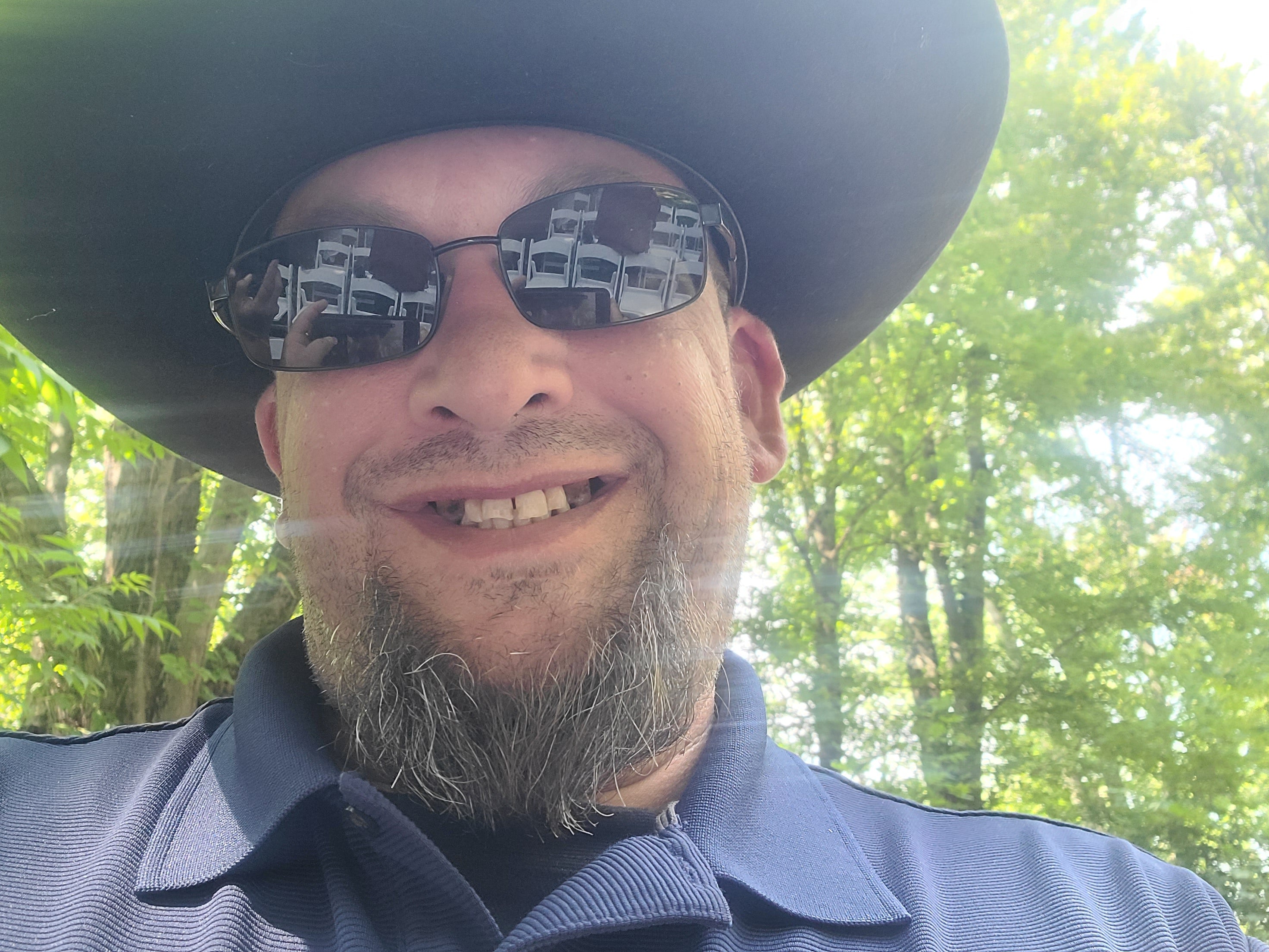 “Mike Wingert outdoors wearing a wide‑brimmed hat and sunglasses, standing in natural sunlight with trees in the background.