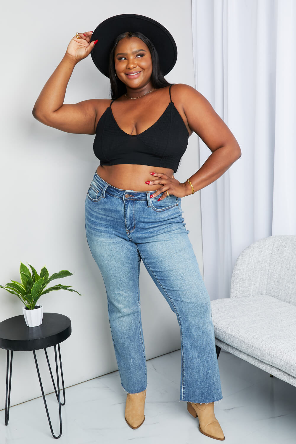 “Model smiling in full outfit with hat and jeans wearing Zenana textured spaghetti strap bralette in black — lifestyle pose