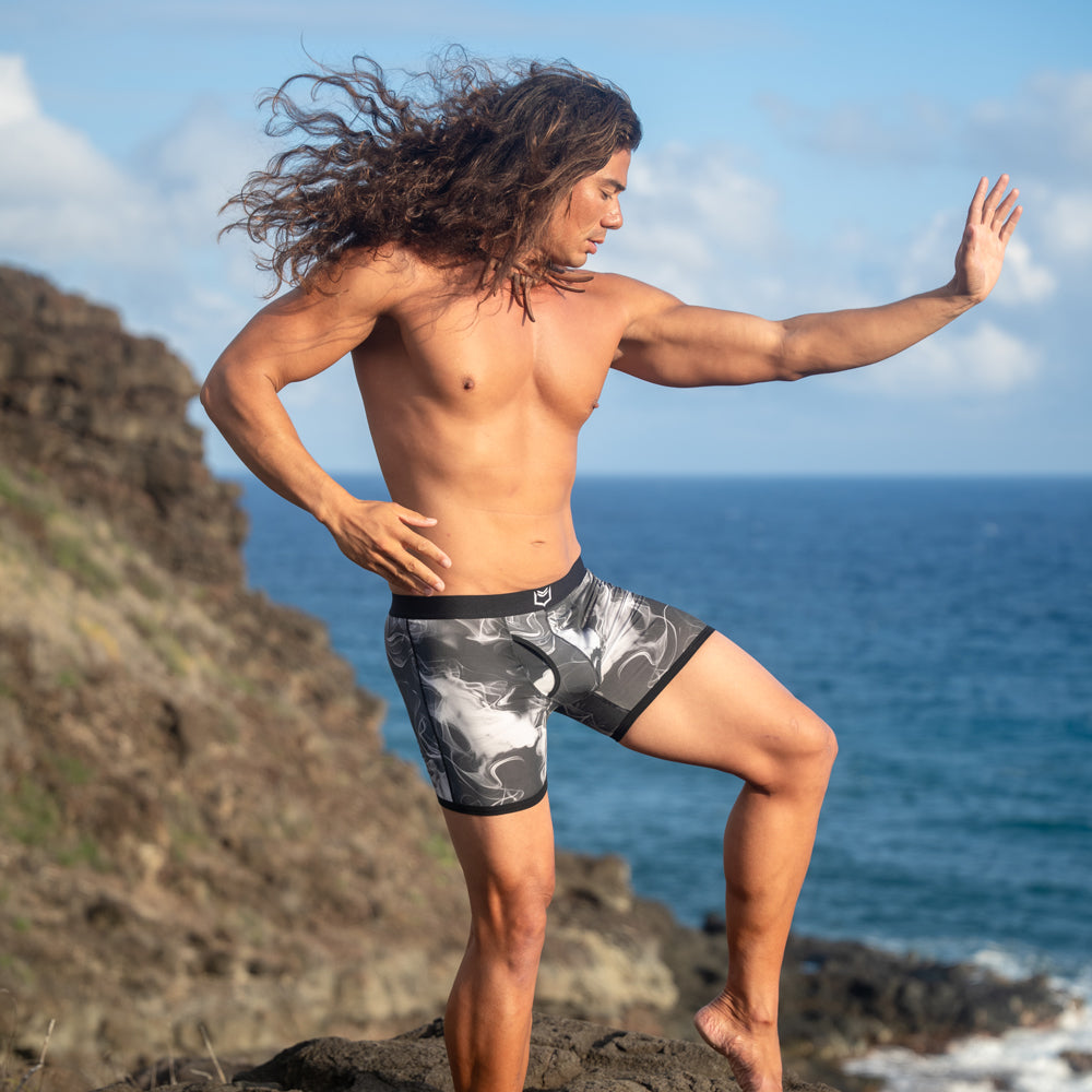 Man wearing men's pouch underwear posing by the ocean on a rocky shore, showcasing style and comfort.