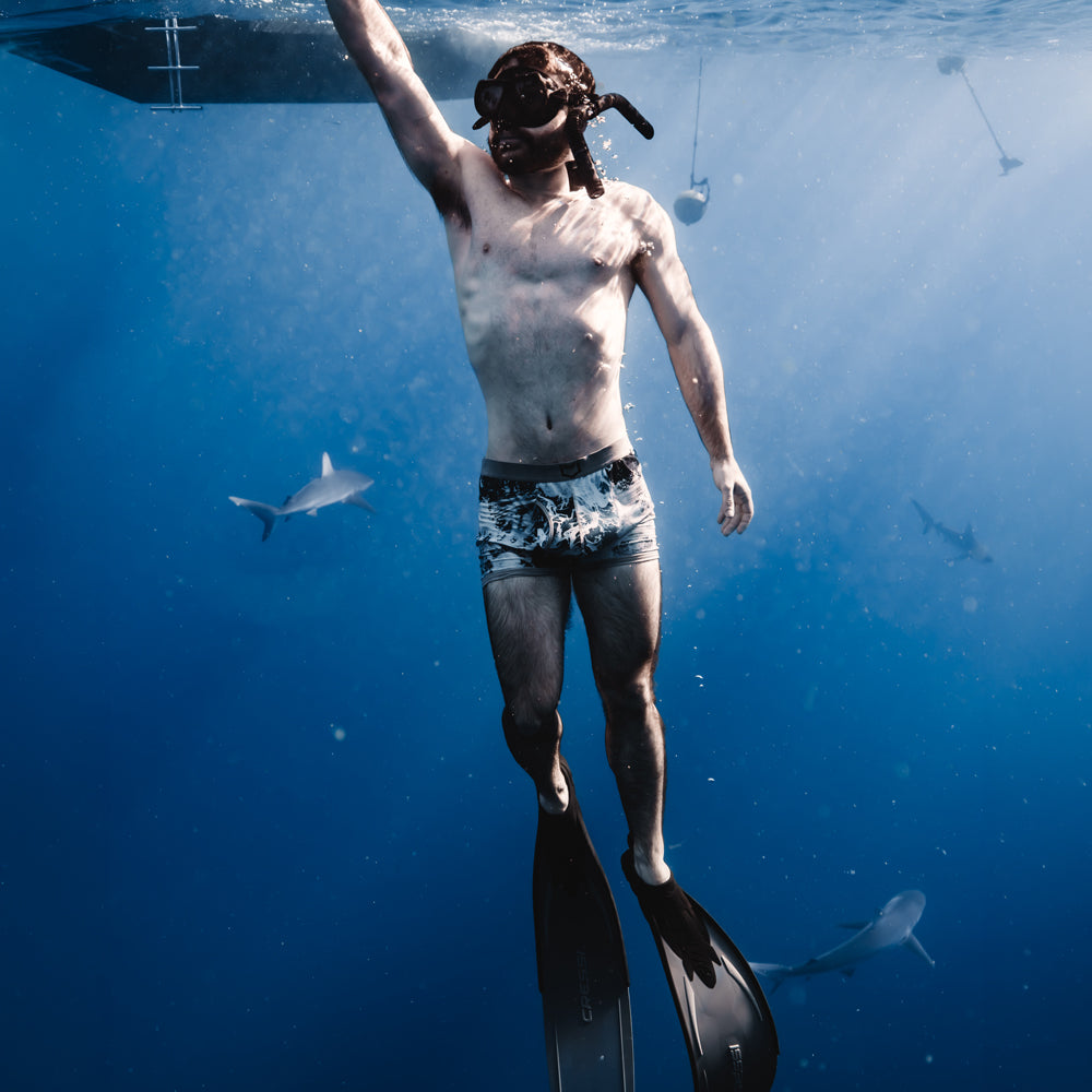 men's pouch underwear Man snorkeling underwater wearing swim trunks and fins, surrounded by marine life.