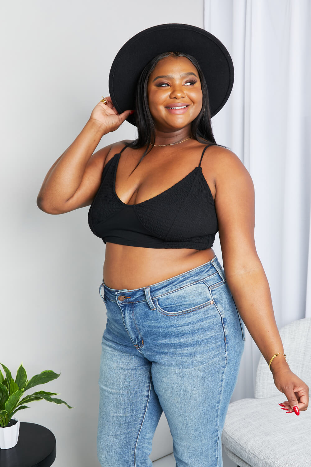 “Lifestyle shot of model smiling in hat and jeans wearing Zenana textured spaghetti strap bralette in black
