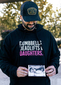 Man wearing a black hoodie with text, holding a ultrasound photo outdoors.
